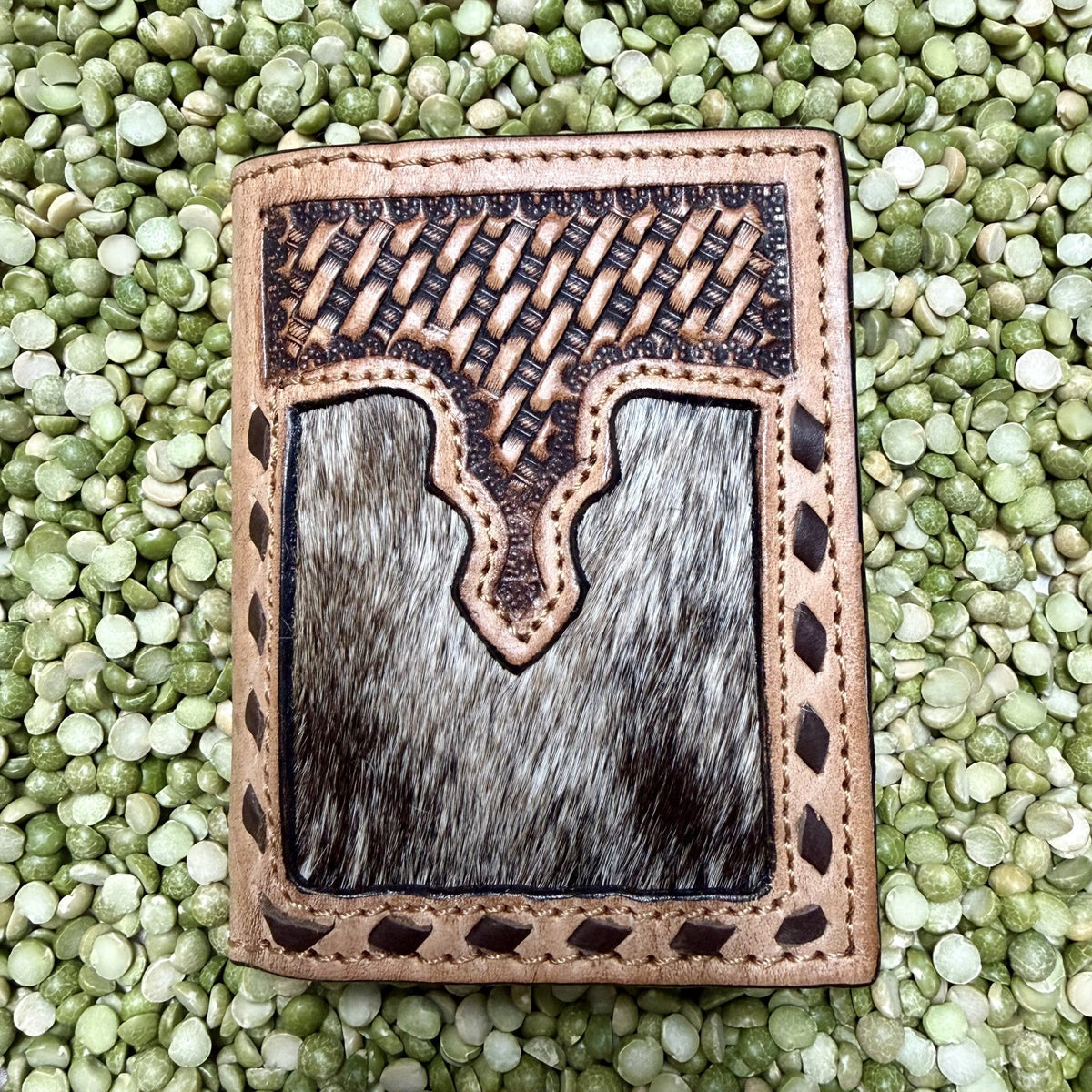 Men's natural-tan trifold wallet with dark basketweave tooling, gray-and-black hair-on-hide front panel, decorative dark lacing, and stitched edges — Blair's Western Wear Marble Falls TX