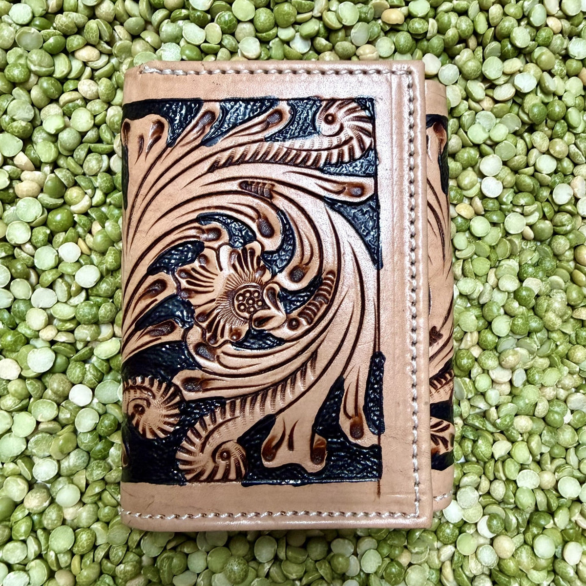 Natural tan leather trifold wallet with floral-scroll tooling, black textured accents, and a stitched border — Blair's Western Wear Marble Falls TX