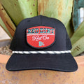 Black cap with red logo patch, turquoise and white lettering, and black-and-white patterned rope trim — Blair's Western Wear Marble Falls TX