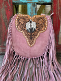 ADBGA431A — This dreamy blush pink suede crossbody is pure boho western romance — long blush fringe on both sides and bottom, a sculpted heart-shaped tan hand-tooled floral leather flap with a single large white and dark gray feather centerpiece, gold diamond whipstitch trim, and a brass D-ring at the top — Blair's Western Wear Marble Falls TX