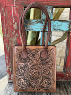 ADBGZ456 — Women's rich tan genuine leather structured tote purse with deep full-coverage floral and scroll hand-tooling, large central daisy/sunflower motif with sweeping acanthus leaf scrollwork and dark brown antiqued contrast, and two sturdy dark brown rounded loop leather top handles — Blair's Western Wear Marble Falls TX