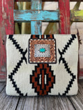 ADBGA286D — Women's handbag with a bold cream and black Navajo-inspired geometric woven front panel with rust/burnt orange accent details, square hand-tooled floral leather frame with silver scalloped oval concho and turquoise oval stone center, brown leather sides, and adjustable tooled leather crossbody strap — Blair's Western Wear Marble Falls TX