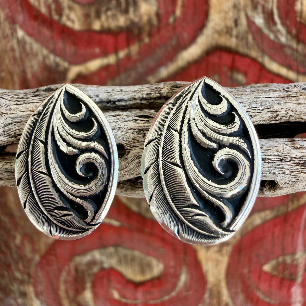 Close-up of silver-tone teardrop earrings showing fine feather lines and raised curling scrollwork contrasted against black recessed detailing — Blair's Western Wear Marble Falls TX