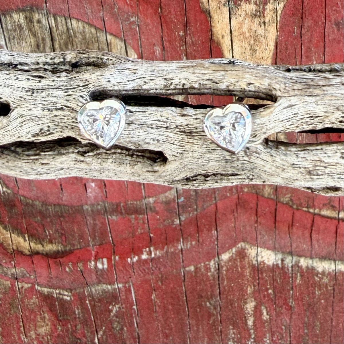 Close-up of women's heart-shaped stud earrings with clear faceted heart centers and polished silver-tone borders — Blair's Western Wear Marble Falls TX