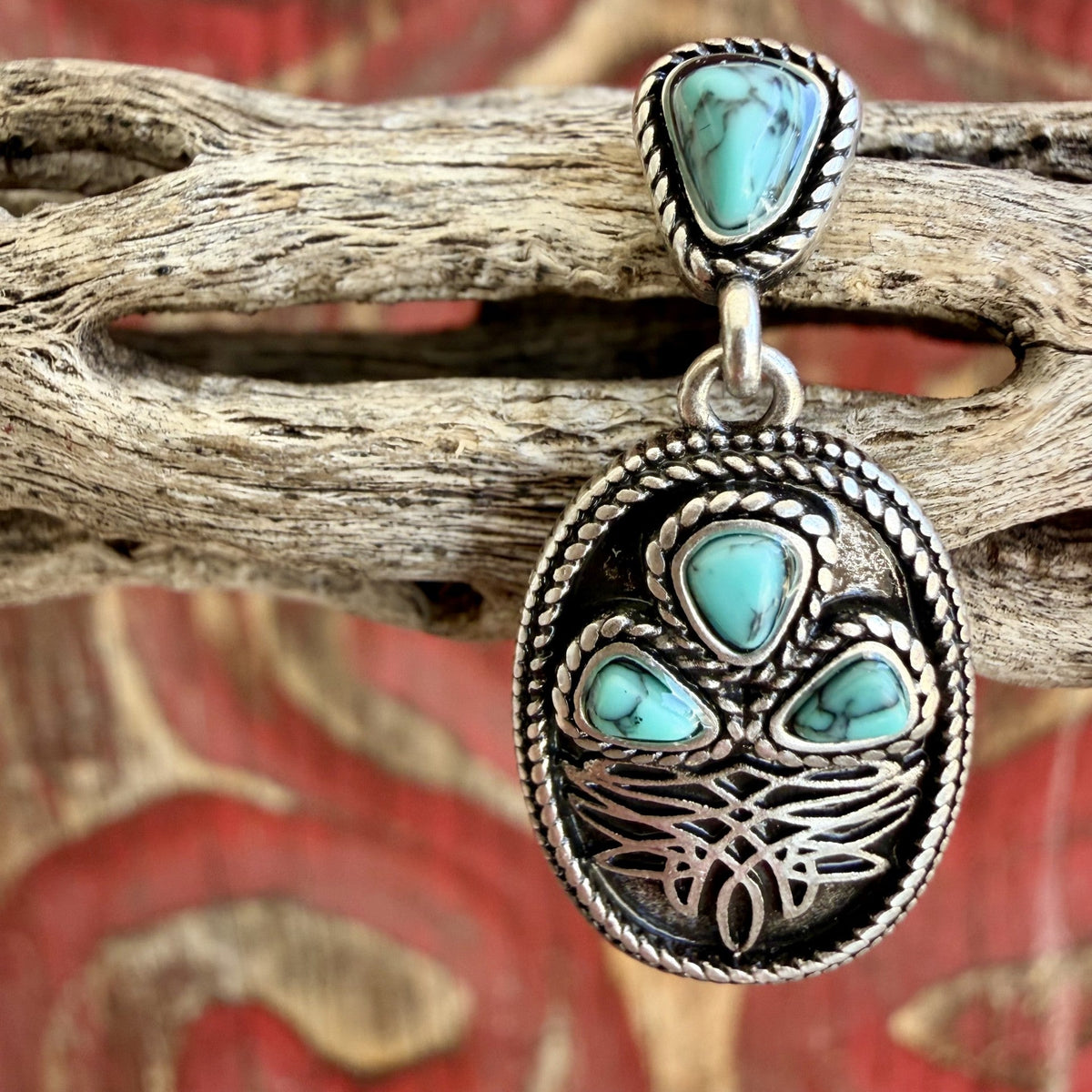 Silver-tone oval earring with dark background, scrolling boot stitch design, rope border, and veined turquoise-colored triangular accents — Blair's Western Wear Marble Falls TX