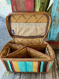 ADBG1320A — Women's structured multicolor serape and cognac leather jewelry and travel vanity case with vibrant vertical serape stripes in turquoise/teal, yellow/gold, brown, black, white, purple, olive green, and rust/red, warm cognac/tan smooth leather edge trim with cream saddle stitching, cognac leather loop carry handle with gunmetal clip on top, and full perimeter zip closure — Blair's Western Wear Marble Falls TX