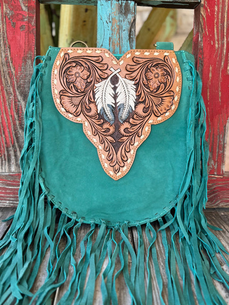 ADBGA431E — This jaw-dropping turquoise suede crossbody has it all — long turquoise fringe on both sides and bottom, a sculpted tan hand-tooled floral leather flap with a painted black and white feather centerpiece, and gold lace whipstitch trim that makes it pure boho western art — Blair's Western Wear Marble Falls TX
