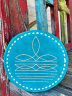 ADBGA620A — Women's round turquoise/teal suede crossbody bag with intricate white western boot toe stitch pattern on the front featuring a central leaf-shaped medallion, three rows of interlocking elongated oval motifs, and horizontal running stitch lines, white diamond whipstitch lacing running the full circumference edge, and perimeter zipper closure — Blair's Western Wear Marble Falls TX